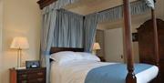 Double bedroom with a canopy bed, beside drawers and a large wooden wardrobe.