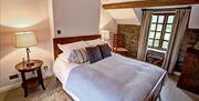 Image shows double bedroom with beside table and lamp, wooden flooring