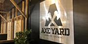 A wooden sign with the Axe Yard logo beside throwing lanes.