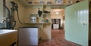 An old tiled kitchen with a water pump, antique cooker and a green door.