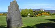 Photo of huge rock set in the green beside the course with club house in the background