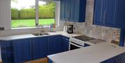 Tiled kitchen with blue cupboards, a hob/oven and a window to the back garden.