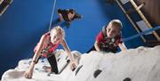 Shows image of children on a climbing wall with a man watching them from down below