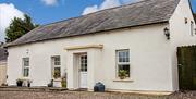 Image shows front of cream painted cottage with flowerbeds on windows and gravel drive