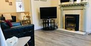 A living room with a fireplace, chair and TV leading to a dining area.