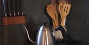 Image of double gas ring hob, with kettle and kitchen utensils in the background.