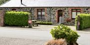 Exterior of stone building. Hedges to both side of gravel area with front door. Ramp and steps.