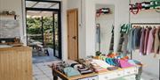 Interior of Bramble Green studio: railings holding a variety of colourful knitted jumpers and a table with knitted hats