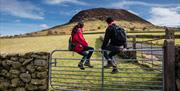 A couple of hikers sitting on a gate admiring the view of Slemish in the background