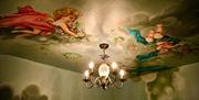 A ceiling with a chandelier light and cherubs painted on the ceiling.