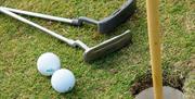 Close up photo of two putting sticks and two golf balls beside putting hole and flag at Seapark