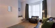 A living room with a leather sofa, armchair, and a bay window with blinds and curtains.