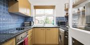 A blue tiled kitchen with a hob/oven, toaster, kettle, sink, microwave, washing machine and dishwasher.