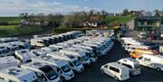 Image of a motorhome show room. 4 rows of motorhomes and campervans are visible.