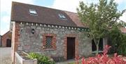 Image shows outside of stone cottage with garden