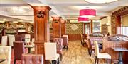 A photo of a large dining room with lots of tables and chairs, wooden pillars and a bar area.