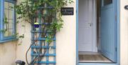 Image shows open front door with trellis to the left of it and Ladybird Cottage sign beside door