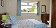 Image shows double bedroom with large window, beside tables, lamps and dressing table with mirror.