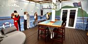 
An outdoor deck featuring murals of people from the Titanic era, wooden furniture, and a seating area with a round couch.