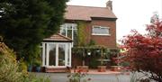 A B&B seen through a colourful garden of trees, bushes and flowers.