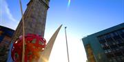 A view looking up at the Albert clock surrounded by buildings from below.