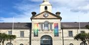 Photograph of the front exterior building of Ards Arts Centre previously the Town Hall, with backdrop of blue sky and two banners flanking the front w