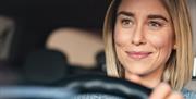 A smiling woman with her hands on the steering wheel of a car.