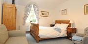 Large double bedroom with a sofa, chair, bedside tables, wardrobe and a large arched window.