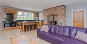 Large open plan kitchen and living room with two ovens, a kitchen island, a woodburning fireplace and a purple corner sofa.