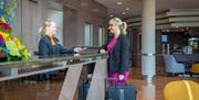 A woman with suitcases being handed her room key at reception.