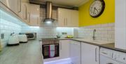 A tiled kitchen with a kettle, toaster, microwave, hob/oven, sink, dishwasher and washing machine.