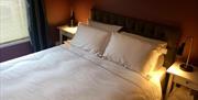 A double bedroom with bedside tables and lit reading lamps against a dark orange wall.