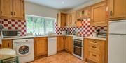 A fully fitted kitchen with red and white tiles, wooden cupboards and a window.