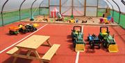 Indoor Soft play area with child sized dumper trucks and a picnic bench