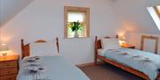 Image shows twin bedroom with beside tables and laps with small window in between beds