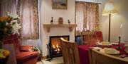 Image shows lounge diner with table and chairs, open fire lit and armchair.