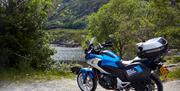 Image shows motorcycle parked at scenic area with view of river between trees