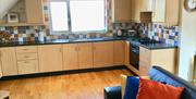 A tiled wall kitchen with a hob/oven, sink and a large window.