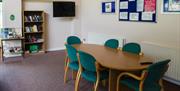 A carpeted room in a building with a TV, table and chairs and a bookcase.