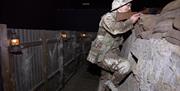 A staged set with a dummy model of a soldier in gear in ditch holding a gun over sandbags on alert