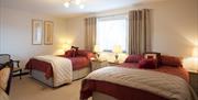 A large bedroom with two double beds, bedside tables, a window and two chairs.