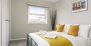 A double bedroom with yellow pillows, folded towels and a window.