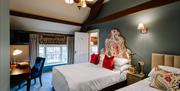 Image shows bedroom with one double bed and one single bed with low window and door to ensuite open