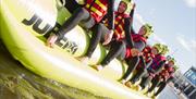 young adults in wet suits sitting on banana boat in the water.