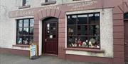 Brown and cream exterior of CF Beattie with sign stating Shooting & Fishing Accessories / Gunsmith plus antique displays in windows