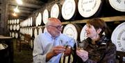 Image of a man and a woman enjoying a drink in the Bushmills Distillery with whiskey barrels behind them