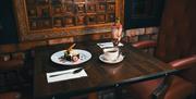 An image showing a wooden table for two with two desserts and a cup of coffee.