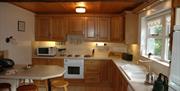 A kitchen with wooden cupboards, a microwave, an oven, a sink and a bench area with stools.