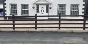 Exterior front view of detached 2 storey dwelling with paved private parking area set back from pavement and road.