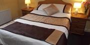 A double bedroom with a brown throw and pillows and nightstands with lamps and flowers.